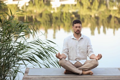 Photo of Man meditating on wooden pier near river. Space for text