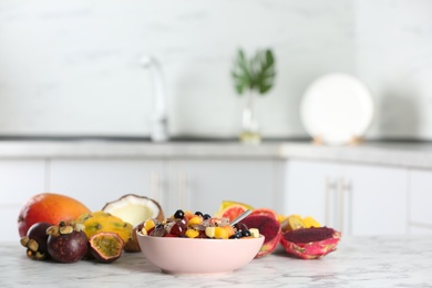 Delicious exotic fruit salad and ingredients on white marble table in kitchen. Space for text