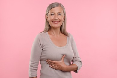 Photo of Beautiful senior woman doing breast self-examination on pink background