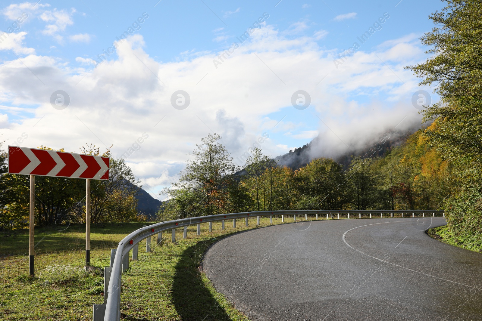 Photo of Picturesque view of empty road near trees with sign Chevron Left in mountains