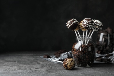 Photo of Yummy cake pops coated with chocolate in glass jar full of coffee beans on table. Space for text