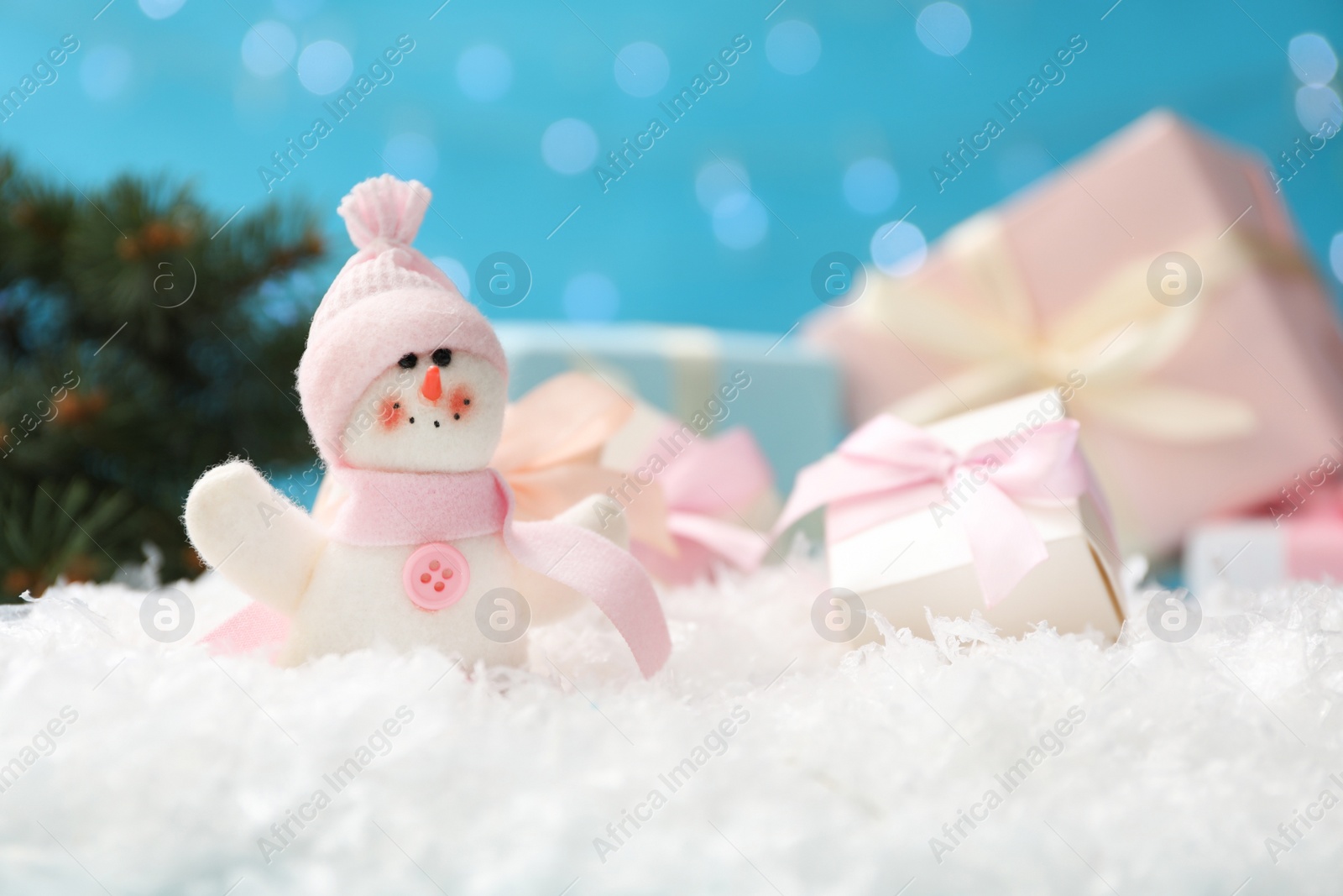 Photo of Cute toy snowman and gift box on snow against blurred background