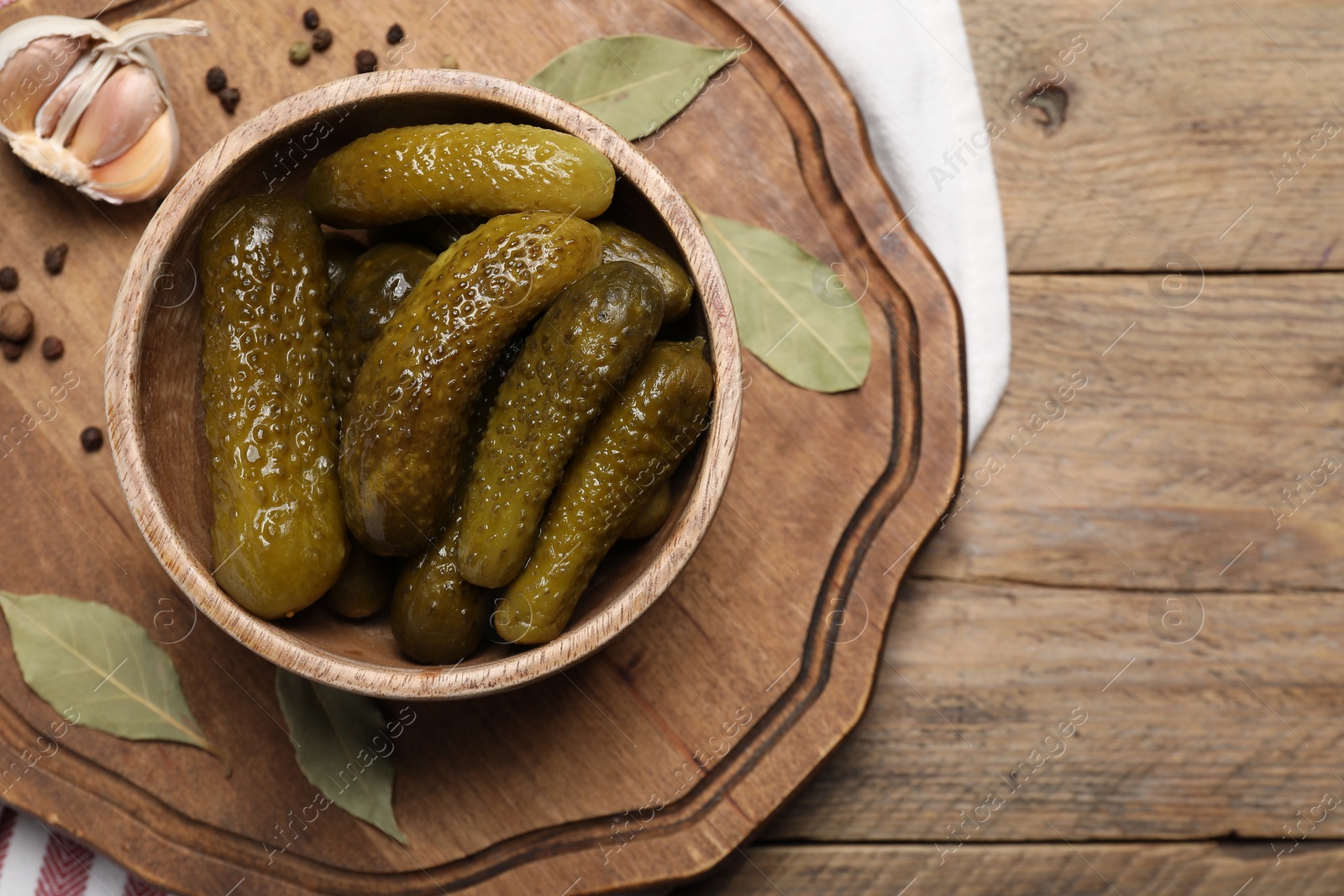 Photo of Tasty pickled cucumbers in bowl and spices on wooden table, flat lay. Space for text