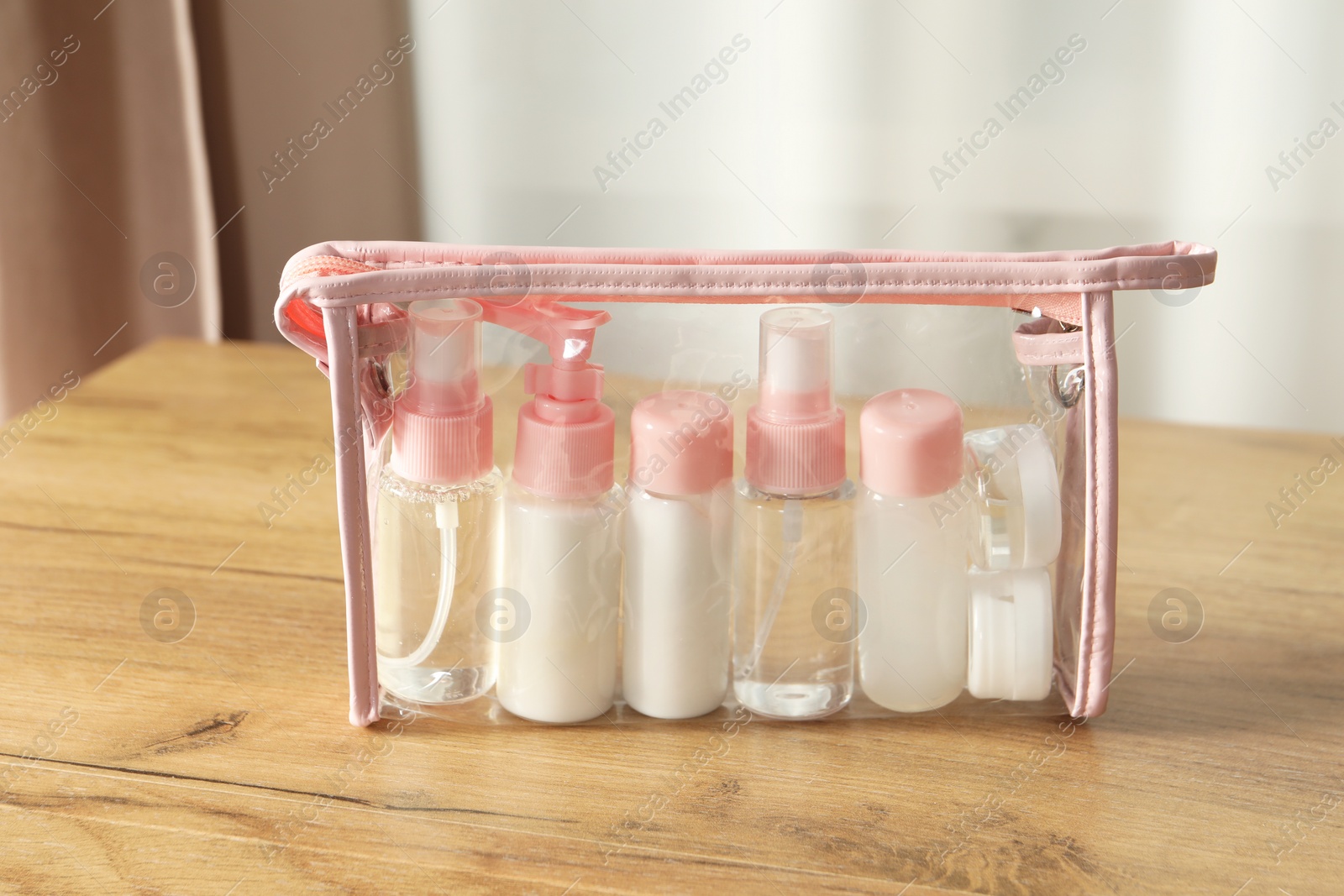 Photo of Cosmetic travel kit. Small containers of personal care products in plastic bag on wooden table indoors