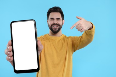Image of Happy man holding smartphone with empty screen on light blue background