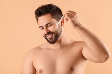 Handsome man applying cosmetic serum onto face on beige background