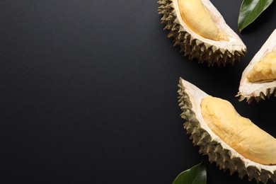 Photo of Pieces of fresh ripe durian and leaves on black background, flat lay. Space for text