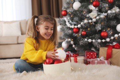 Cute little girl with box of Christmas balls at home