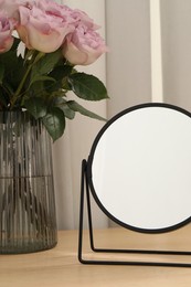 Photo of Mirror and vase with pink roses on wooden dressing table, closeup