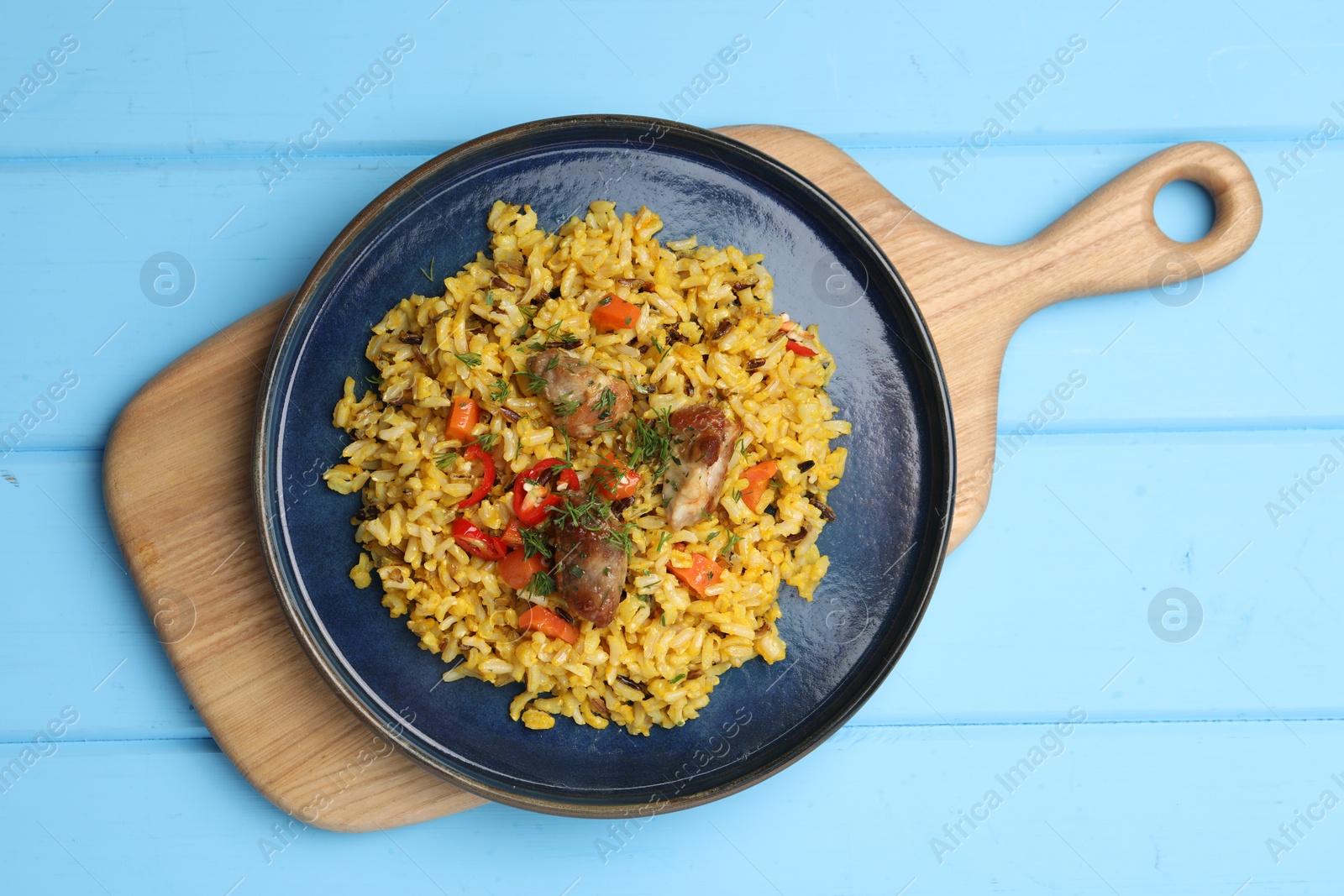 Photo of Delicious pilaf with meat, carrot and chili pepper on light blue wooden table, top view