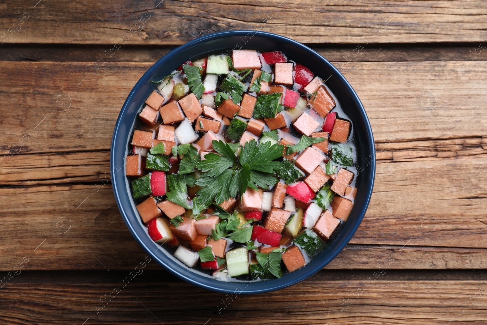 Photo of Delicious cold okroshka with kvass on wooden table, top view. Traditional Russian summer soup