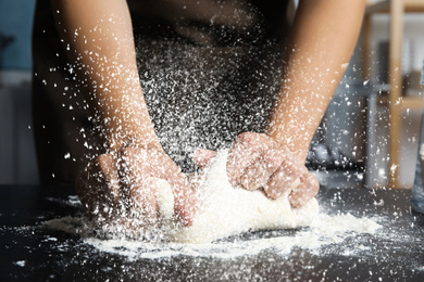 Young woman kneading dough at table in kitchen, closeup