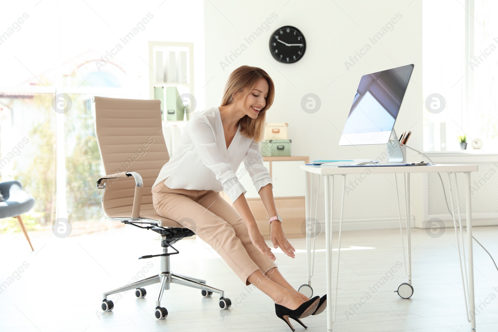 Photo of Young beautiful businesswoman stretching in office. Workplace fitness