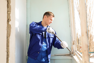 Worker dismantling old window with crowbar indoors