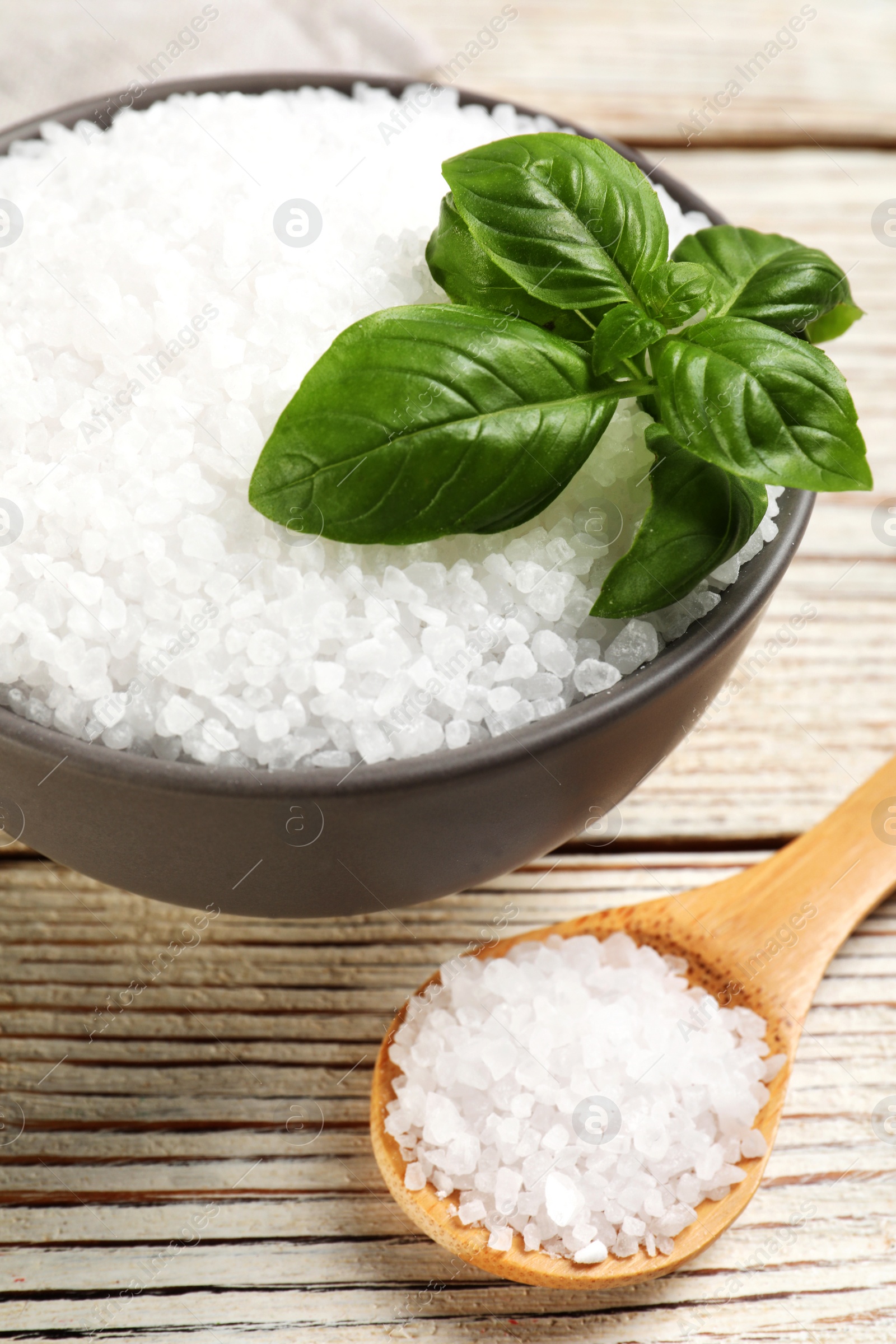 Photo of Bowl and spoon with natural sea salt on white wooden table, closeup