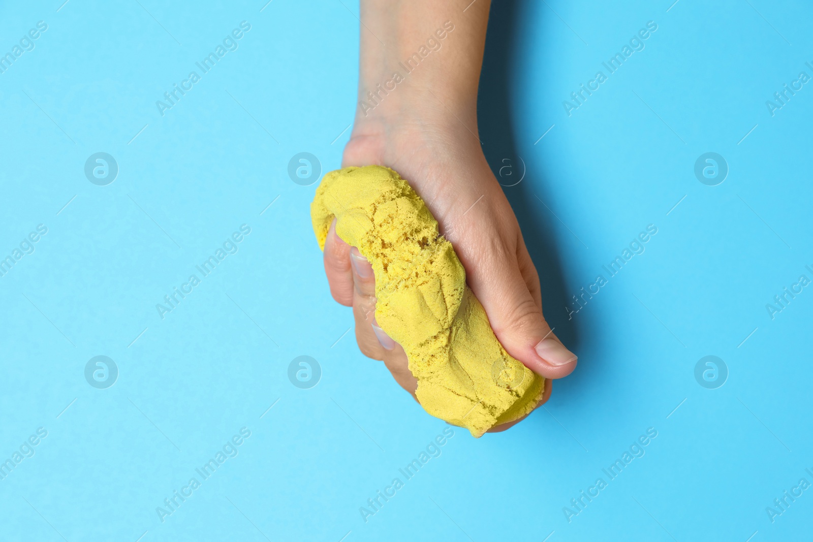 Photo of Woman playing with yellow kinetic sand on light blue background, top view