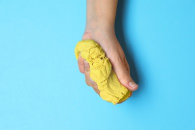 Woman playing with yellow kinetic sand on light blue background, top view