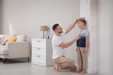 Father measuring height of his son near wall at home