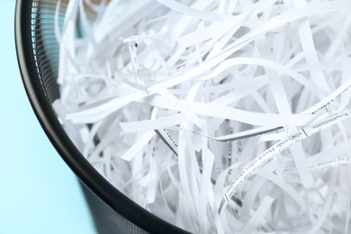 Trash bin with shredded paper strips on light blue background, closeup