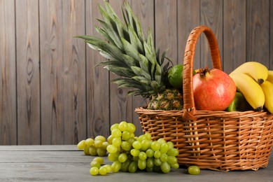 Photo of Wicker basket with different ripe fruits on wooden table. Space for text