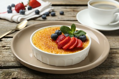 Photo of Delicious creme brulee with berries and mint in bowl on wooden table, closeup