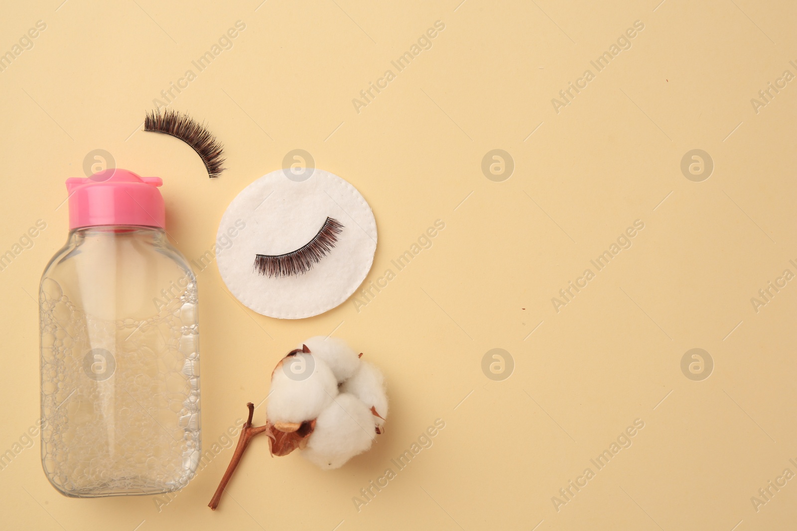 Photo of Bottle of makeup remover, cotton flower, pad and false eyelashes on yellow background, flat lay. Space for text