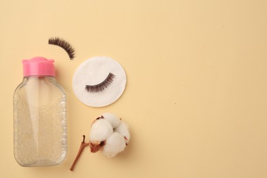 Bottle of makeup remover, cotton flower, pad and false eyelashes on yellow background, flat lay. Space for text