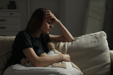 Photo of Sad young woman sitting on sofa at home