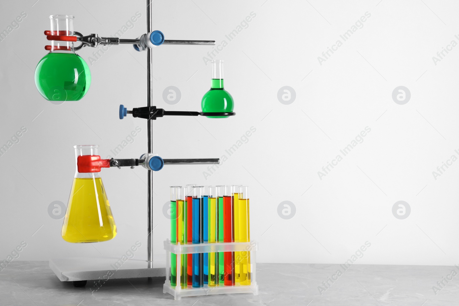 Photo of Retort stand and laboratory glassware with liquids on grey table against white background, space for text