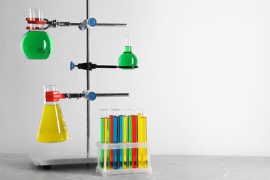 Photo of Retort stand and laboratory glassware with liquids on grey table against white background, space for text