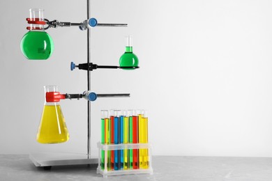 Retort stand and laboratory glassware with liquids on grey table against white background, space for text