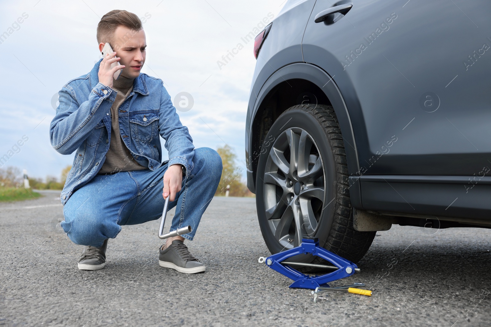 Photo of Worried young man calling car service. Tire puncture