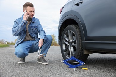 Photo of Worried young man calling car service. Tire puncture