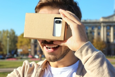 Young man using cardboard virtual reality headset outdoors