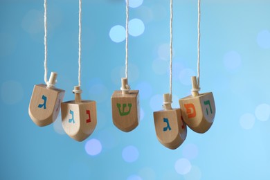 Photo of Hanukkah celebration. Wooden dreidels with jewish letters hanging on twine against light blue background with blurred lights