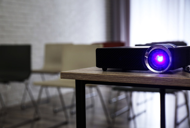 Photo of Modern video projector on wooden table in conference room. Space for text