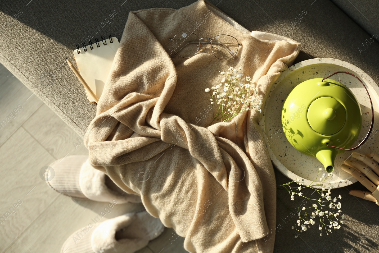 Photo of Soft cashmere sweater, tea pot and flowers on sofa, flat lay