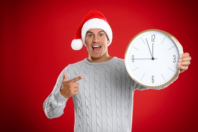 Man in Santa hat with clock on red background. Christmas countdown