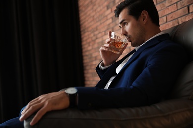 Photo of Young man with glass of whiskey near brick wall indoors. Space for text