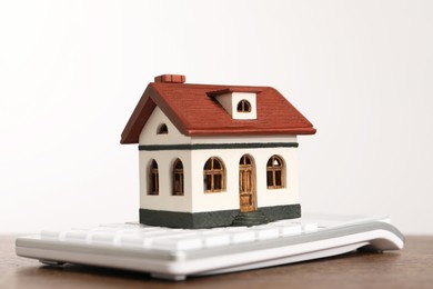Mortgage concept. House model and calculator on wooden table against white background, closeup
