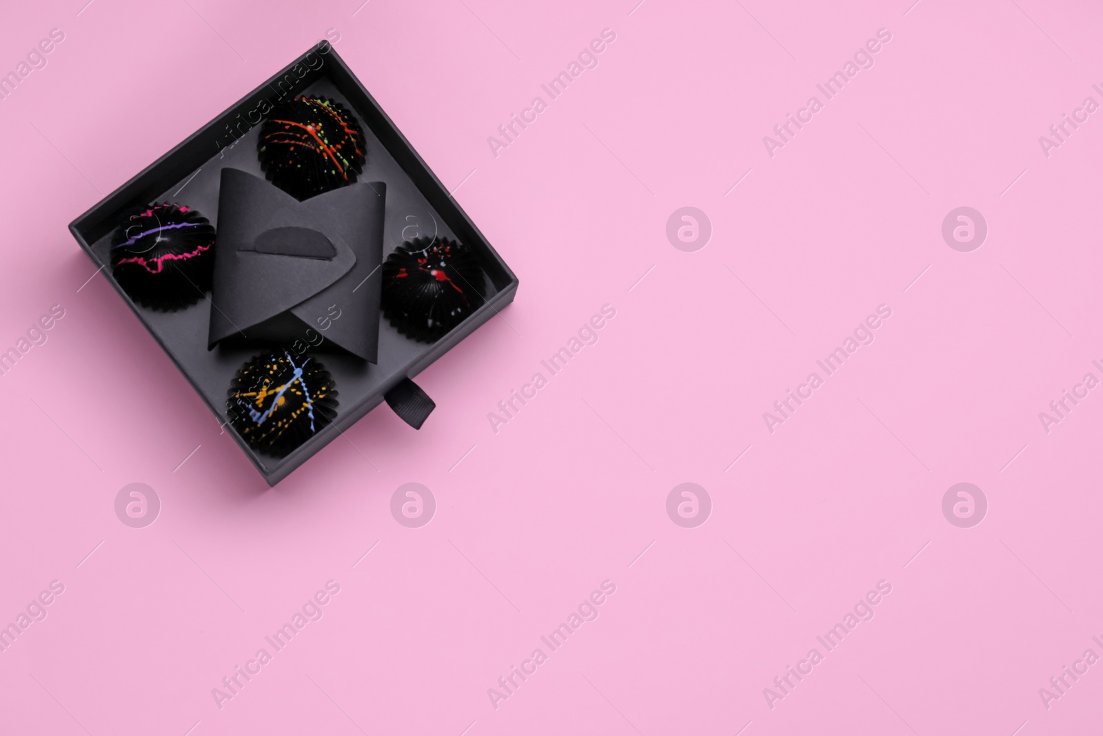 Photo of Box of tasty chocolate candies on pink background, top view. Space for text