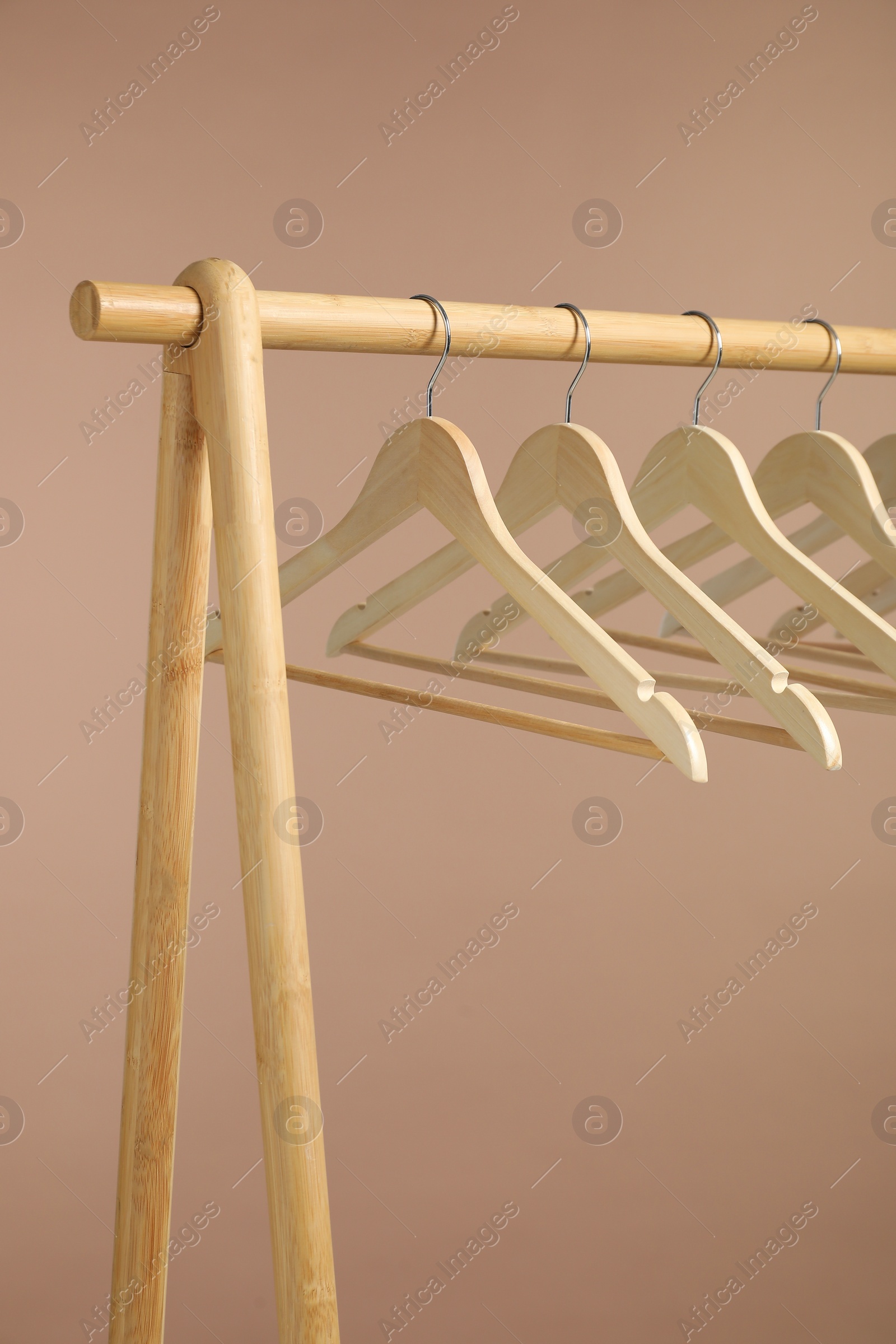 Photo of Empty clothes hangers on wooden rack against light brown background