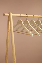 Photo of Empty clothes hangers on wooden rack against light brown background