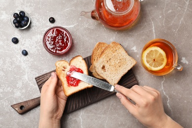 Photo of Woman spreading jam on toast against grey background