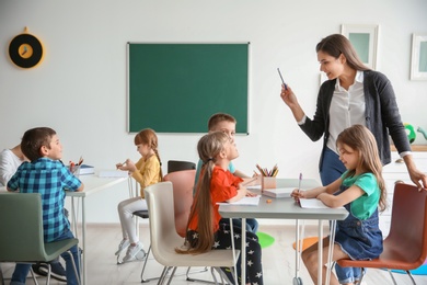 Photo of Cute little children with teacher in classroom at school