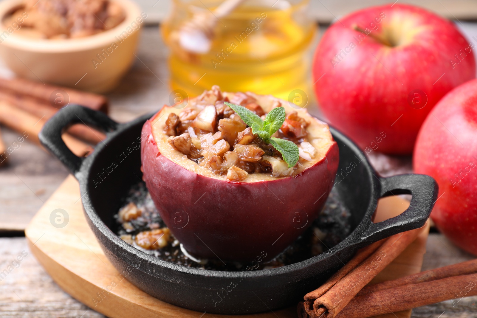 Photo of Tasty baked apple with nuts in baking dish and cinnamon sticks on wooden table, closeup