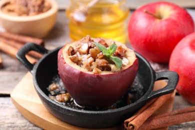 Tasty baked apple with nuts in baking dish and cinnamon sticks on wooden table, closeup