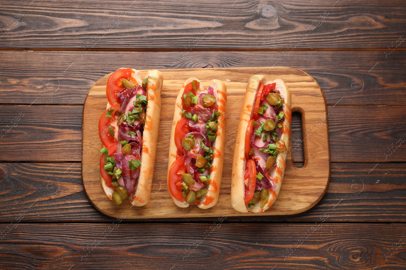 Photo of Tasty hot dogs with green onion, tomato, pickles and sauce on wooden table, top view