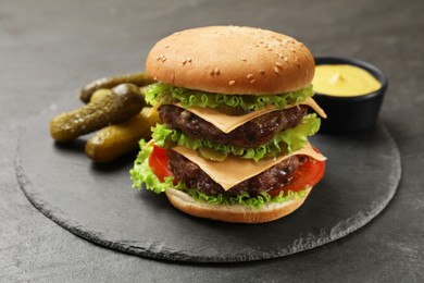 Tasty hamburger with patties, pickles and sauce on black table