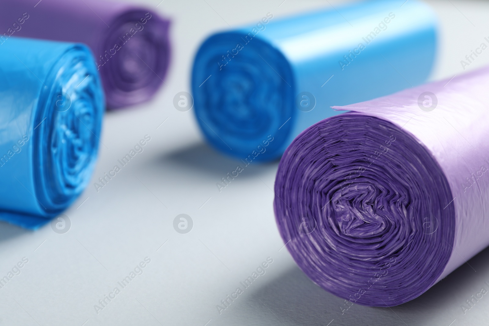 Photo of Rolls of different color garbage bags on light background, closeup